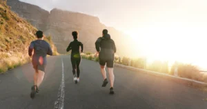 Fitness, corsa e sport con gli amici in montagna per sfide cardio o di performance. Esercizio, allenamento o formazione con gli atleti su strada asfaltata nella natura